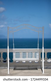 White Porch Swing On The Boardwalk Overlooking The Blue Sea