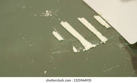 A white powder being lined on the table. Using a white sheet of hard paper a bunch of white powder is being cut into pieces and lined on the table