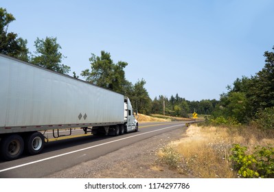 White powerful big rig semi truck tractor transporting goods in dry van semi trailer going uphill on spectacular winding road between the hills with dried grass and mist of hot summer air