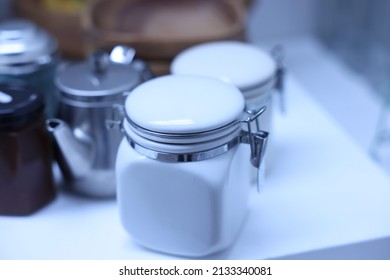 White preserve jars and other kitchen utensils sitting on a white kitchen counter top.