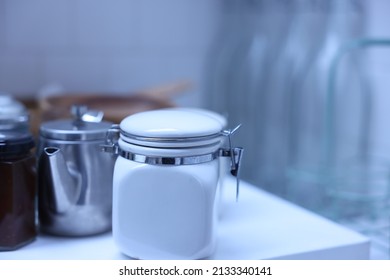 White preserve jars and other kitchen utensils sitting on a white kitchen counter top.