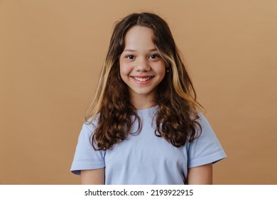 White preteen girl wearing t-shirt smiling and looking at camera isolated over beige background