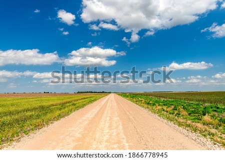 White, puffy clouds moving over remote dirt road and flat lands in the Great Plains, Oklahoma.