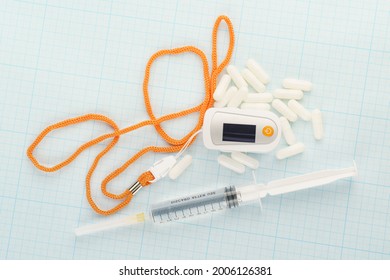 White Pulse Oximeter, Capsules And Syringe On Graph Paper Background. Outpatient Therapy, Condition Monitoring, Drug Therapy And Covid Treatment Theme