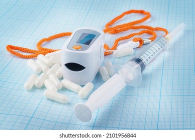 White Pulse Oximeter, Capsules And Syringe On Graph Paper Background. Outpatient Therapy, Condition Monitoring, Low Angle View, Therapy And Covid Treatment Theme