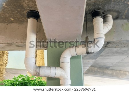 White pvc drain pipes below the parking garage building in Destin, Florida. Views of drainage pipe near the concrete painted pillar from below.