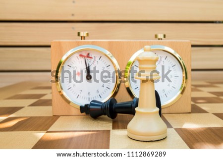 white queen in front of fallen black king and chess clock