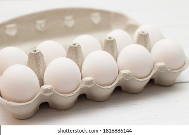 White raw chicken eggs in egg carton box on white wooden background. Selective focus.