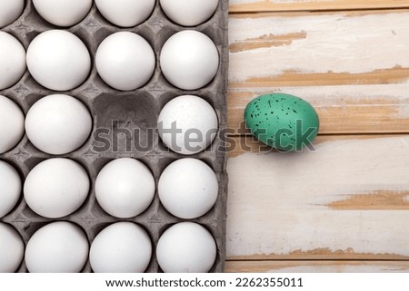 white raw eggs in a container and one colored Easter egg. Preparing for the holiday of light Easter. View from above. Space for text.