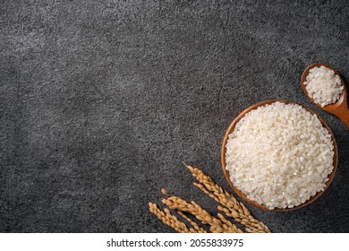 White raw rice in a bowl with the ear on the dark black table background.