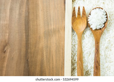 white raw Thai jasmine rice in wooden box with brown wooden fork and spoon on wood table, close up, copy space