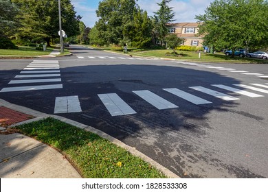 White rectangular intermittent crosswalk markers painted on the asphalt road in a residential neighborhood