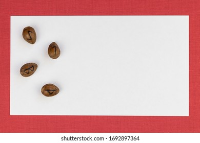 White rectangular sheet of paper lies on red fabric, on the left edge of the paper are four runes (futark), burnt on apricot kernels. Horizontal mockup with place for text.