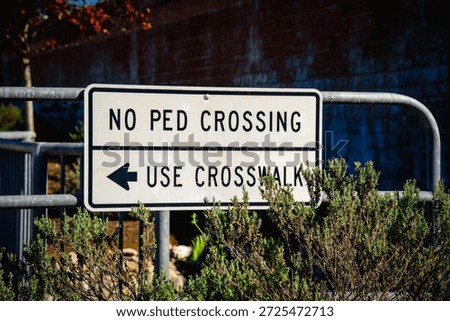 A white rectangular sign with black lettering indicates 'NO PED CROSSING' and 'USE CROSSWALK' with an arrow pointing left