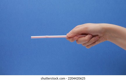 White And Red Bendy Straw Pointed Forward In Hand On A Blue Background