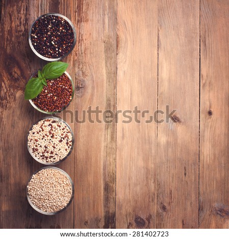 White, red, black and mixed raw quinoa, South American grain, in glass bowls on old rustic woodenbackground. Top view. Background with copy space. Toned.
