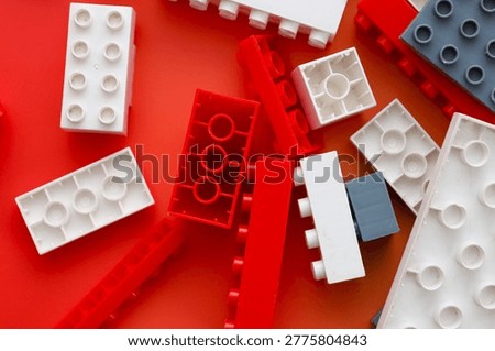 White, red, and gray plastic construction details are chaotically scattered on a bright red background. This high-contrast composition perfectly illustrates concepts of early childhood development, creative building,