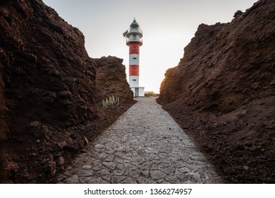 White and red lighthouse between two rock walls with a concrete pathway at sunset