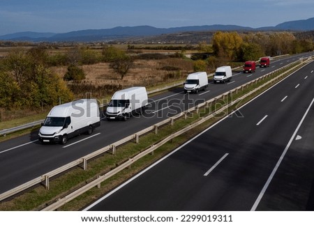 White and red minivans are moving in a convoy on the highway.  White and red modern delivery small shipment cargo courier van moving fast on motorway road to city urban suburb.