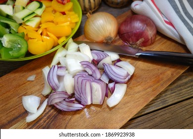 White and red onions cut on a wooden board. Vegetables on a plate in the background. Preparation of the dish - letcho