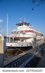 A white and red riverboat docked along the blue waters of the Savannah River with blue sky and clouds in Savannah Georgia USA