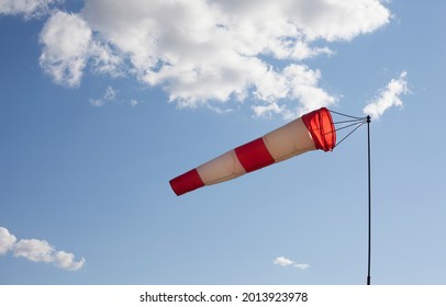 White and red wind flag (windsock) with blue sky background. Air sleeve on a sunny day indicating direction of wind. Windy weather concept.