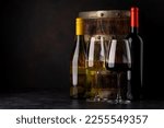 White and red wine bottles in front of wine barrel