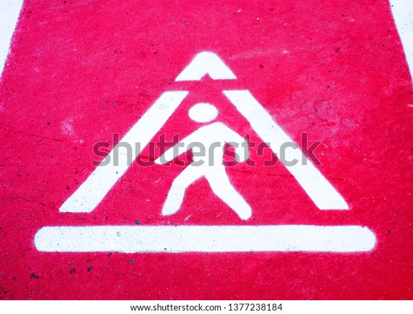 White reflective sign, pedestrian crossing\
symbol, painted on bright red\
pavement.