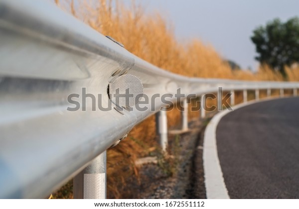White reflective sign warn curve at\
night on the steel guard rail on the road in day\
time.