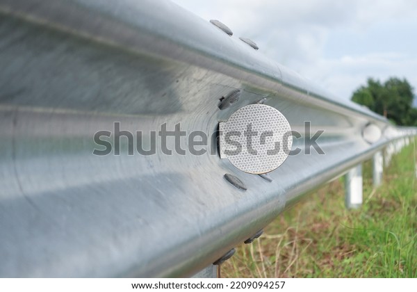 White reflective sign warn curve at night on\
the steel guard rail on the street road in the countryside with\
green grass close-up.