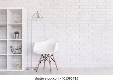 White Regale With Home Decorations, Standing Lamp And Modern Chair Standing In Light Room With Brick Wall Design