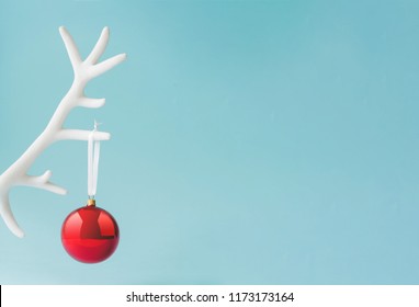 White reindeer antler with red Christmas bauble decoration on pastel blue background. New Year minimal concept.