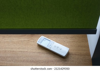 White Remote Control Panel For Motorized Roller Shades Or Automatic Blinds Lies On A Wooden Windowsill Near The Window.