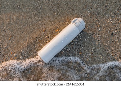 White reusable steel stainless thermo water bottle on sand on sea beach. Flask thermos of drinks for resting and relax
