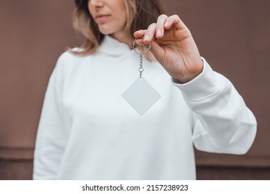 White rhombus keychain mockup in woman's hand. Blank white sublimation keychain. Copy space.