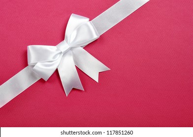White ribbon with bow on a pink background