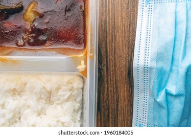 White Rice And Bbq Chicken In Plastic Container And Blue Face Mask On A Wooden Table. Take Away Dinner At Covid 19 Pandemic Cocnept