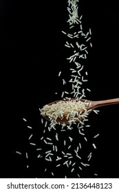 White rice grains falling down into the spoon at black background. Popular food and main ingredient of risotto and pilau.
