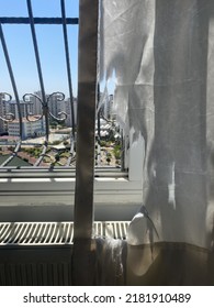 White Ripped Curtain Torn In Front Of A Window With Black Metal Grate