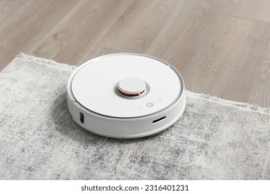 Robot blanco aspiradora sobre la alfombra en la sala de estar cerca del sofá. Limpieza del apartamento con una moderna y elegante aspiradora.