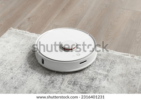 White robot vacuum cleaner on the carpet in the living room near the sofa. Cleaning the apartment with a modern smart vacuum cleaner. Сток-фото © 