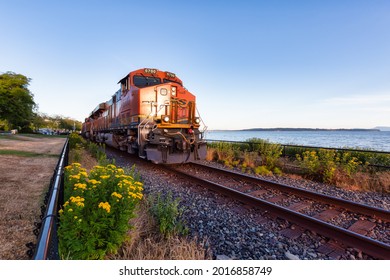 White Rock, Greater Vancouver, British Columbia, Canada - July 25, 2021: A freight train riding through the city by the beach during a colorful summer evening.