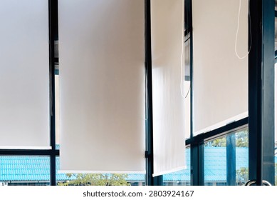 White roller blinds installed on large windows of modern room. Inside view of grey fabric roller blinds or shades installed on big glass windows providing sun protection in contemporary interior.