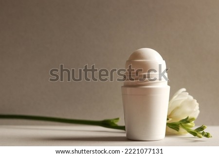 White roll-on antiperspirant deodorant bottle on a gray background with freesia branch. Skin care concept. Copy space.