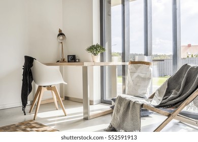 White room with deckchair, wooden desk, chair and window wall