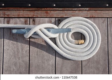 White rope coiled on a wooden dock and tied to a metal cleat.  
