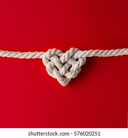 White Rope In Heart Shape Knot On Red Background. Love Concept. Flat Lay.