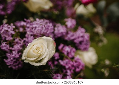 White rose with raindrops in a vibrant arrangement of lilac and foliage, capturing a fresh and romantic floral detail.