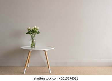 White Roses In Glass Vase  On Small Round Table Against Beige Wall