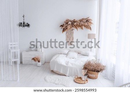 White round bed with macrame and dried plants creating cozy bohemian interior design in a bright bedroom with a white floor and white curtains
